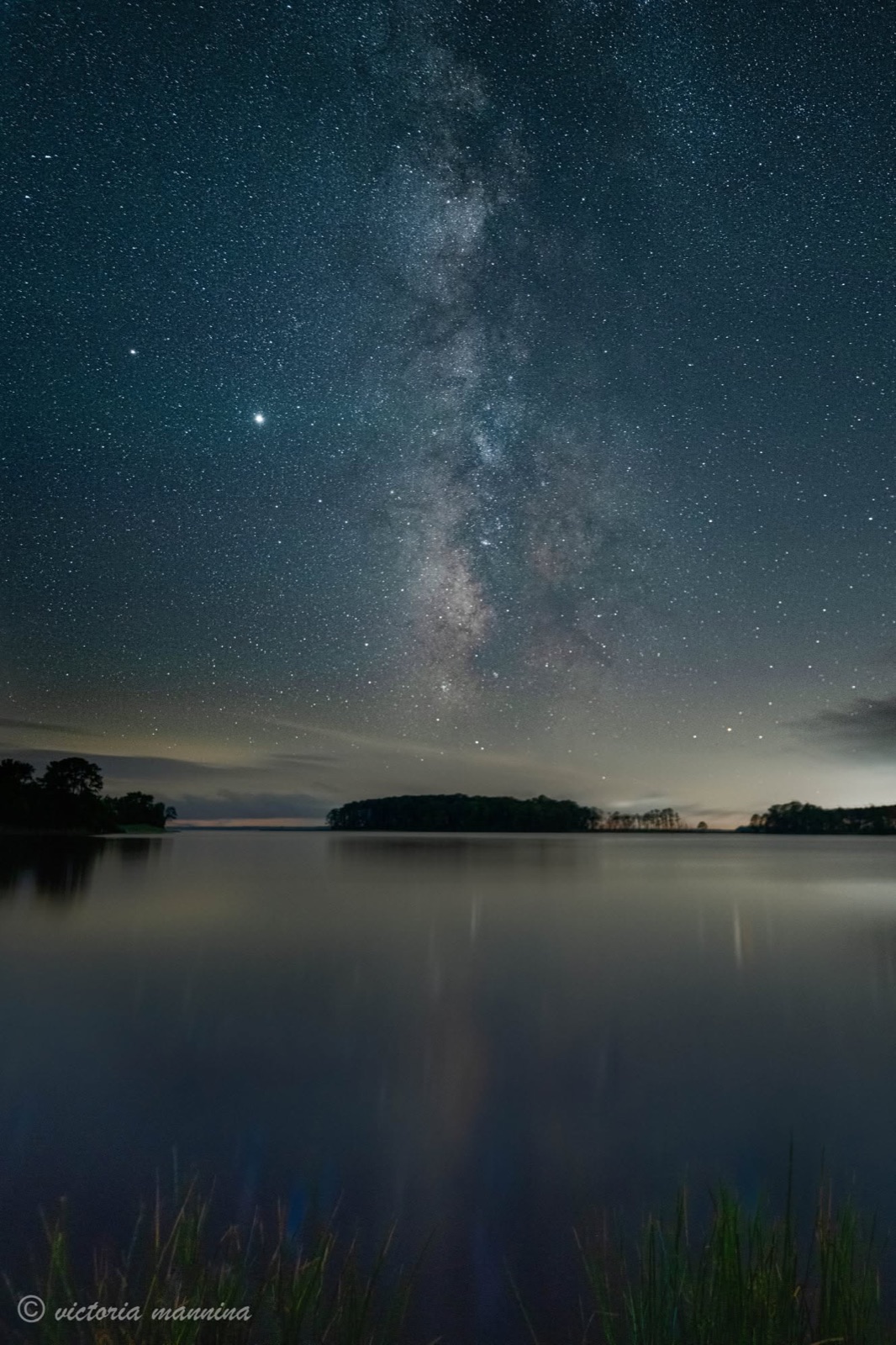 Milky Way and bright planets reflected over calm water