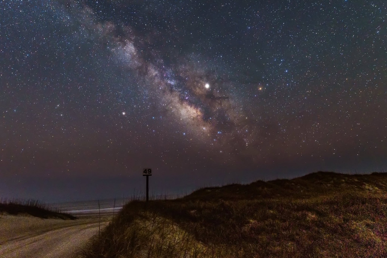 Striped Cape Hatteras lighthouse beaming light under the Milky Way