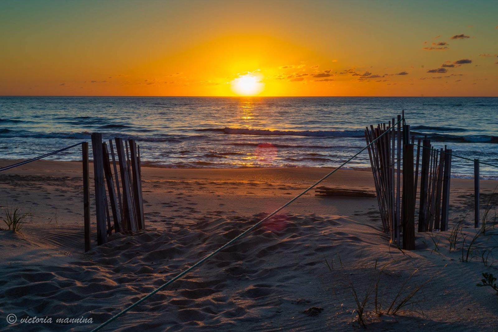 Sun rising over the ocean framed by a wooden beach fence