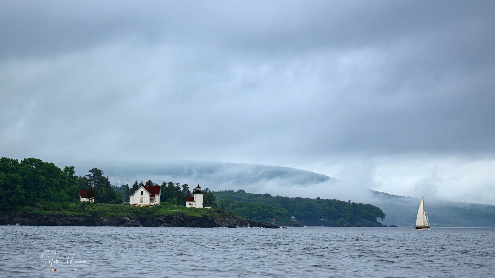 White lighthouse and keeper's house on foggy coastal point, sailboat passing